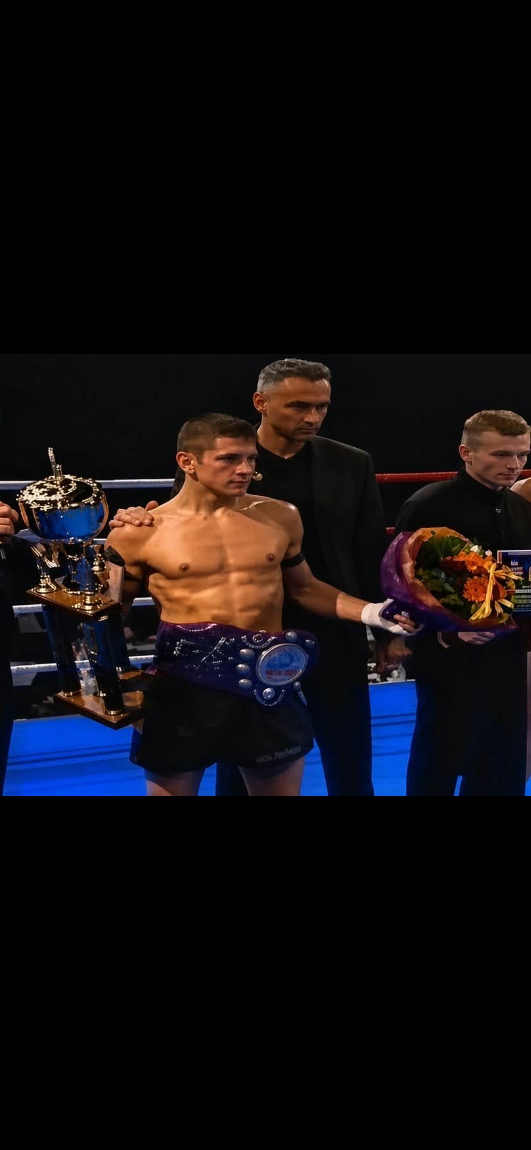 Dennis Købke in the ring with a championship belt, trophy and flowers.